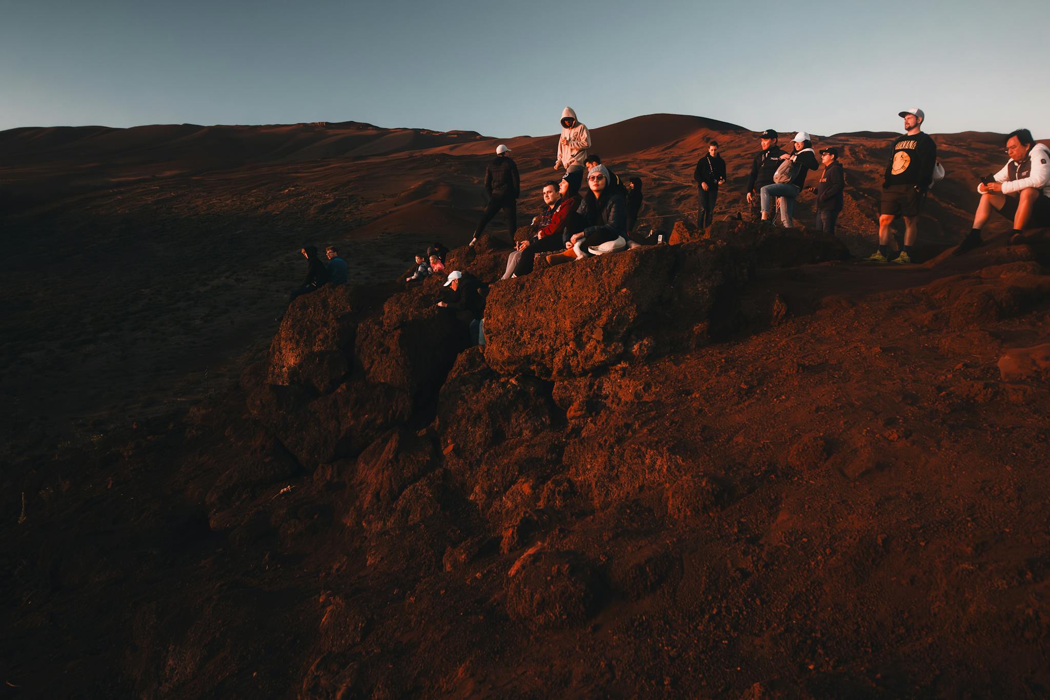 A group of hikers enjoys a sunset view on rocky terrain in Hawaii.